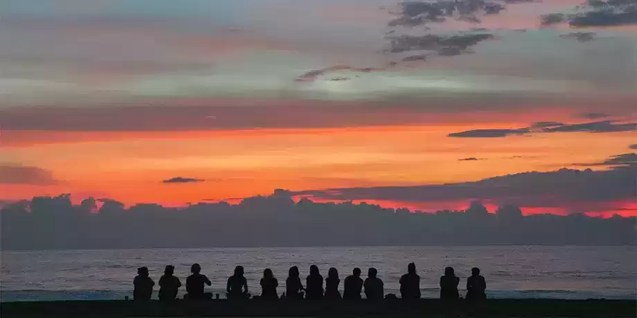 Youth sitting in a line facing the sea looking at the sunset