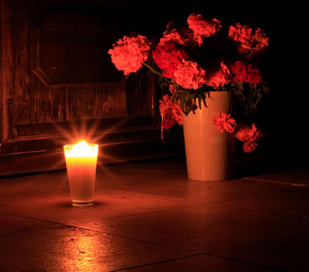 a candle and a bouquet of flowers in a dark room in memory of the deceased of the family