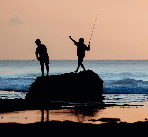 Children standing on a rock fishing in the ocean
