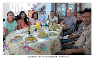 Columban Fr. John Boles sits at a table with a family in Peru