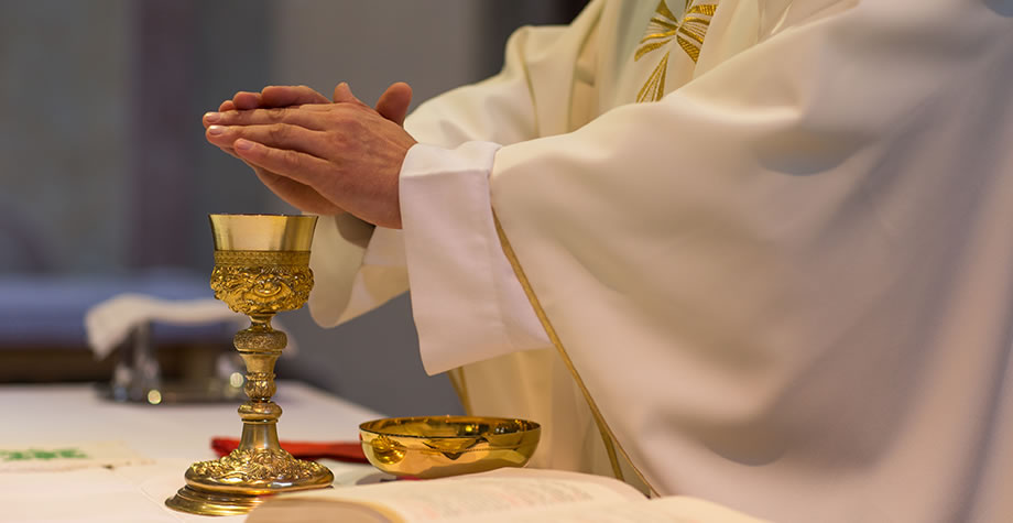 A priest at the altar with hands folded over the chalice