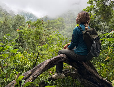 Young woman with backpack rests on fallen tree in lush jungle landscape