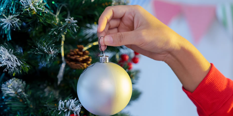 A hand hanging an ornament on a Christmas Tree