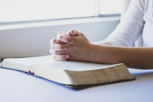 hands clasped on an open bible