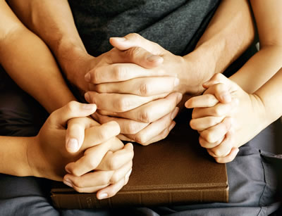Hands clasped over Bible in family prayer