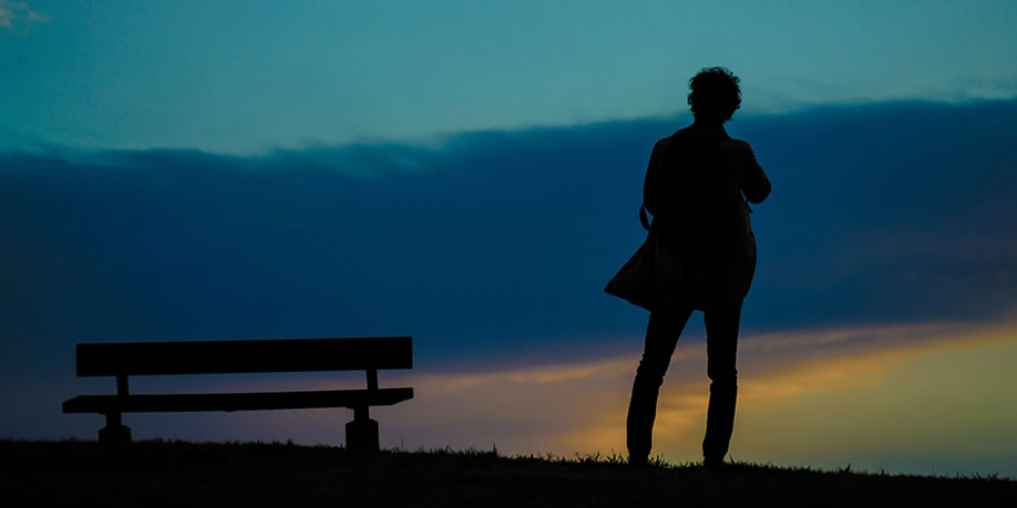 Solitary person standing on a hillside near a park bench