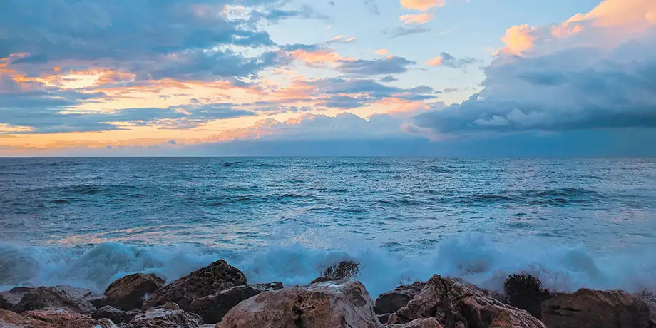 Ocean waves batter a rocky shore at dusk