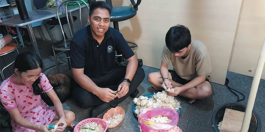 Columban student Matang Moeniba from Kiribati helping a family peel garlic for sale.