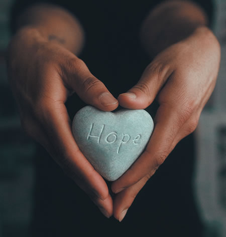 Hands holding a heart-shaped stone with the word hope on it.