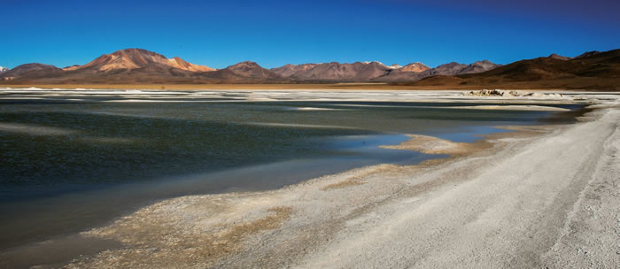 A barren dry mountainous land surrounds a drying lake