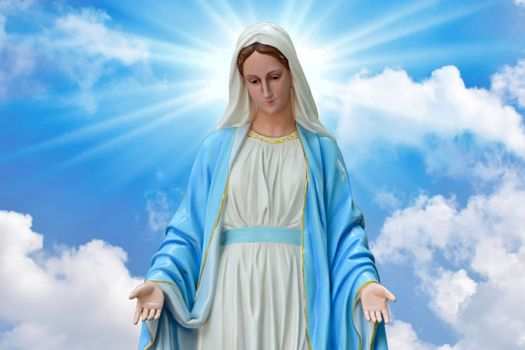 Statue of the Blessed Virgin Mary in front of a blue sky with puffy clouds.
