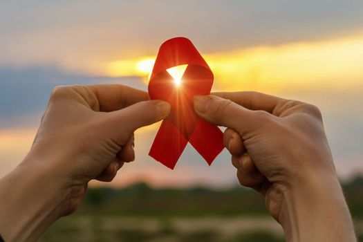 AIDS red ribbon in hands on the background of a sunset.