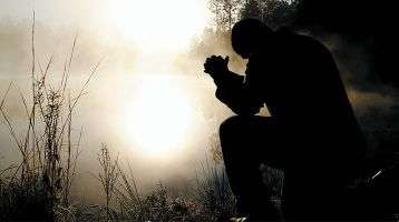 Man kneeling in prayer in the early dawn.