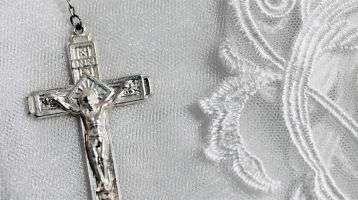 A silver crucifix of a rosary setting on white lace