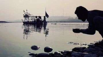 A man kneeling by a lake hands cupped with lake water.