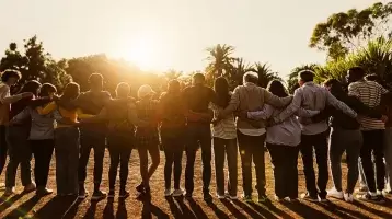 A group of people with arms interlocked facing the rising sun