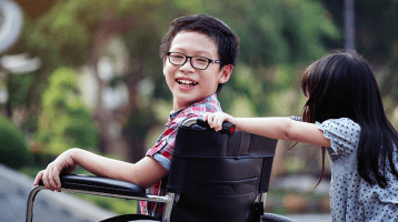 Child in a wheel chair being pushed by another child on a school playground