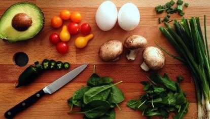 Avacado, onions, tomatos, eggs, mushrooms and leafy greens on a cutting board