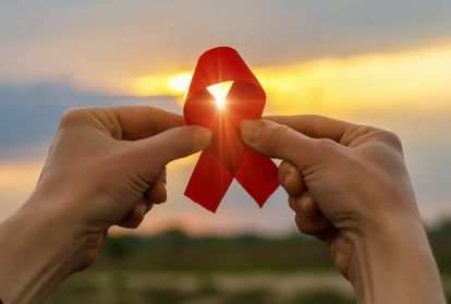 AIDS red ribbon in hands on the background of a sunset.