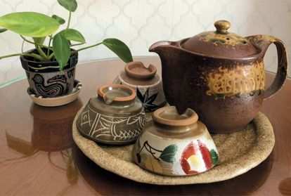 A table with a potted plant and a tray with a teapot and three small cups