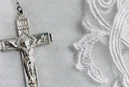 A silver crucifix of a rosary setting on white lace