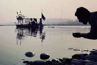 A man kneeling by a lake hands cupped with lake water.