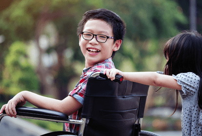 Child in a wheel chair being pushed by another child on a school playground