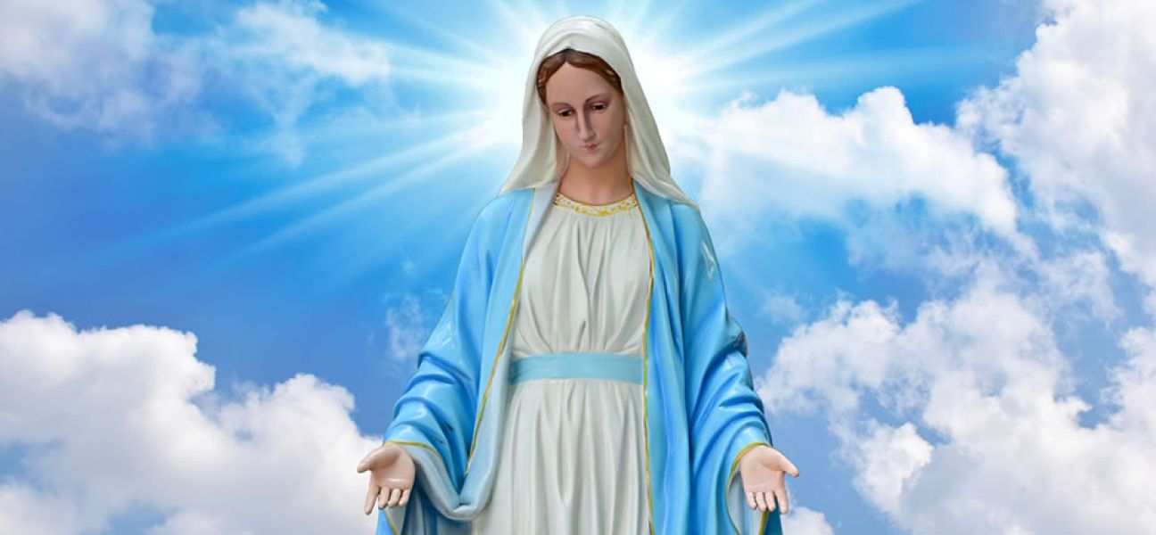 Statue of the Blessed Virgin Mary in front of a blue sky with puffy clouds.