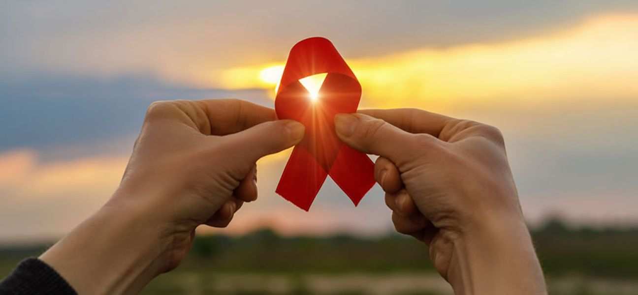 AIDS red ribbon in hands on the background of a sunset.