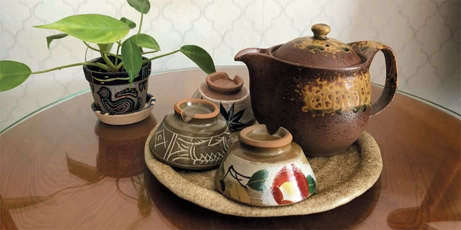 A table with a potted plant and a tray with a teapot and three small cups