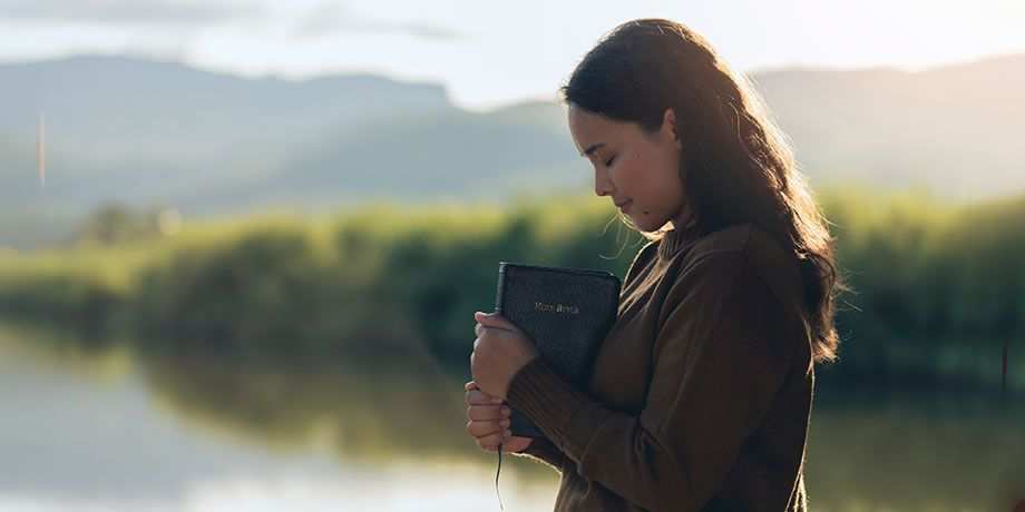 A young women near a lake holding a bible in reflection and thanks.