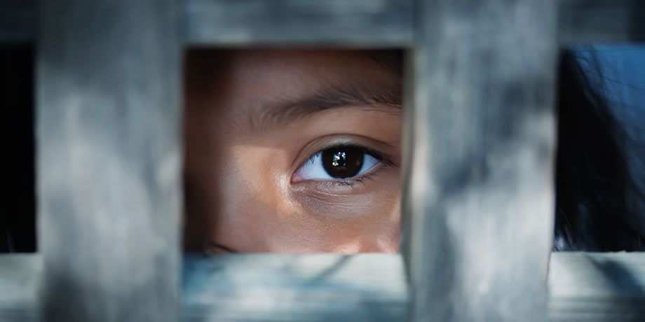 The blank stare of a child's eye who is standing behind wooden cage.