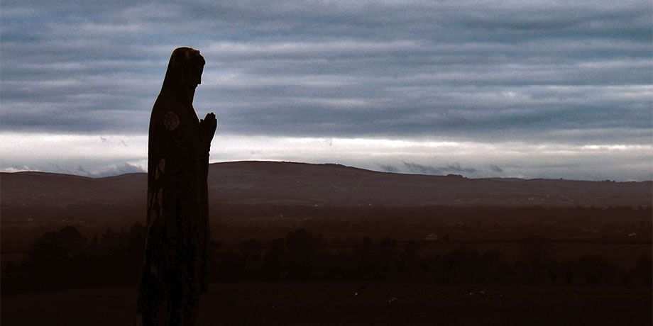 A statue of Mary overlooks the cemetary at dusk.