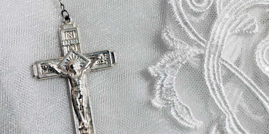 A silver crucifix of a rosary setting on white lace