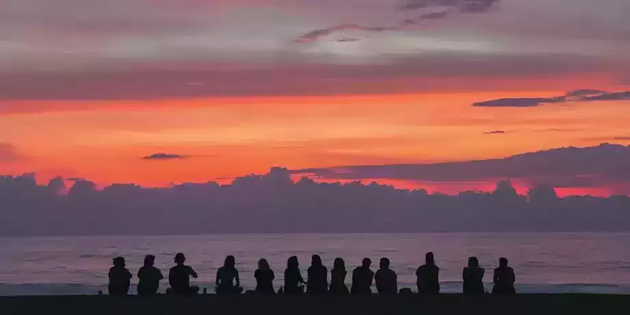 Group of people sitting on a beach at sunset
