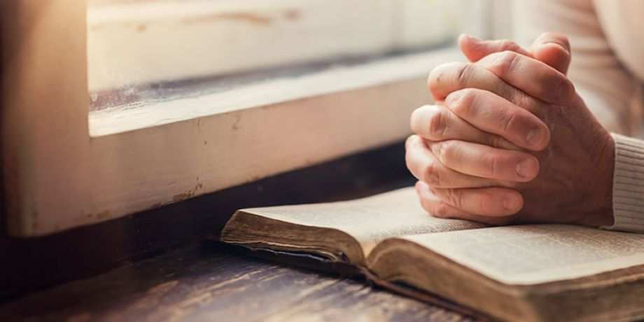 Hands clasped in prayer on a bible.