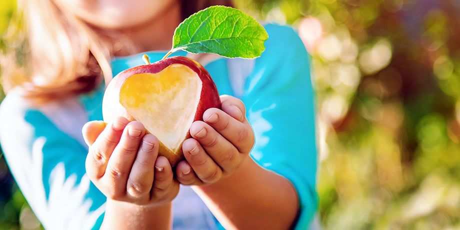 A child holds out an apple with a heart carved out of it.