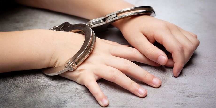 A childs hands in handcuffs rest on a table.
