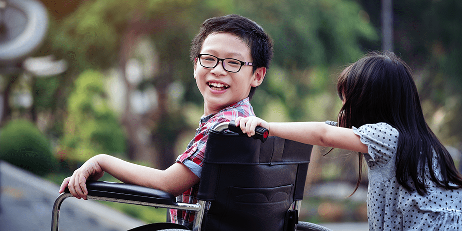 Child in a wheel chair being pushed by another child on a school playground