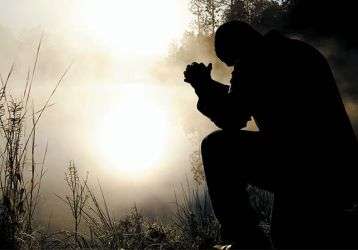 Man kneeling in prayer in the early dawn.