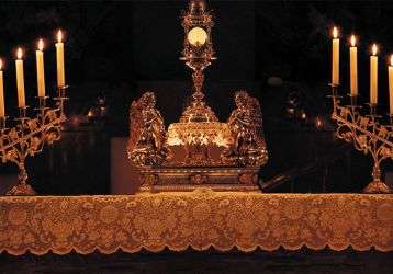 The Exposition of the Blessed Sacrament on the altar with candles lit .