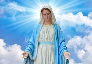 Statue of the Blessed Virgin Mary in front of a blue sky with puffy clouds.