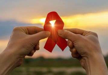 AIDS red ribbon in hands on the background of a sunset.