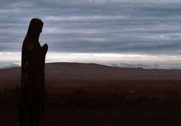 A statue of Mary overlooks the cemetary at dusk.