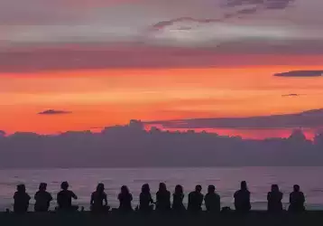 Group of people sitting on a beach at sunset