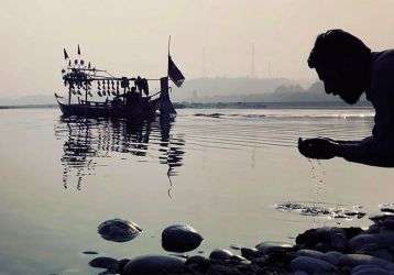 A man kneeling by a lake hands cupped with lake water.