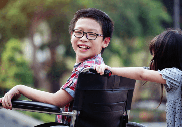 Child in a wheel chair being pushed by another child on a school playground